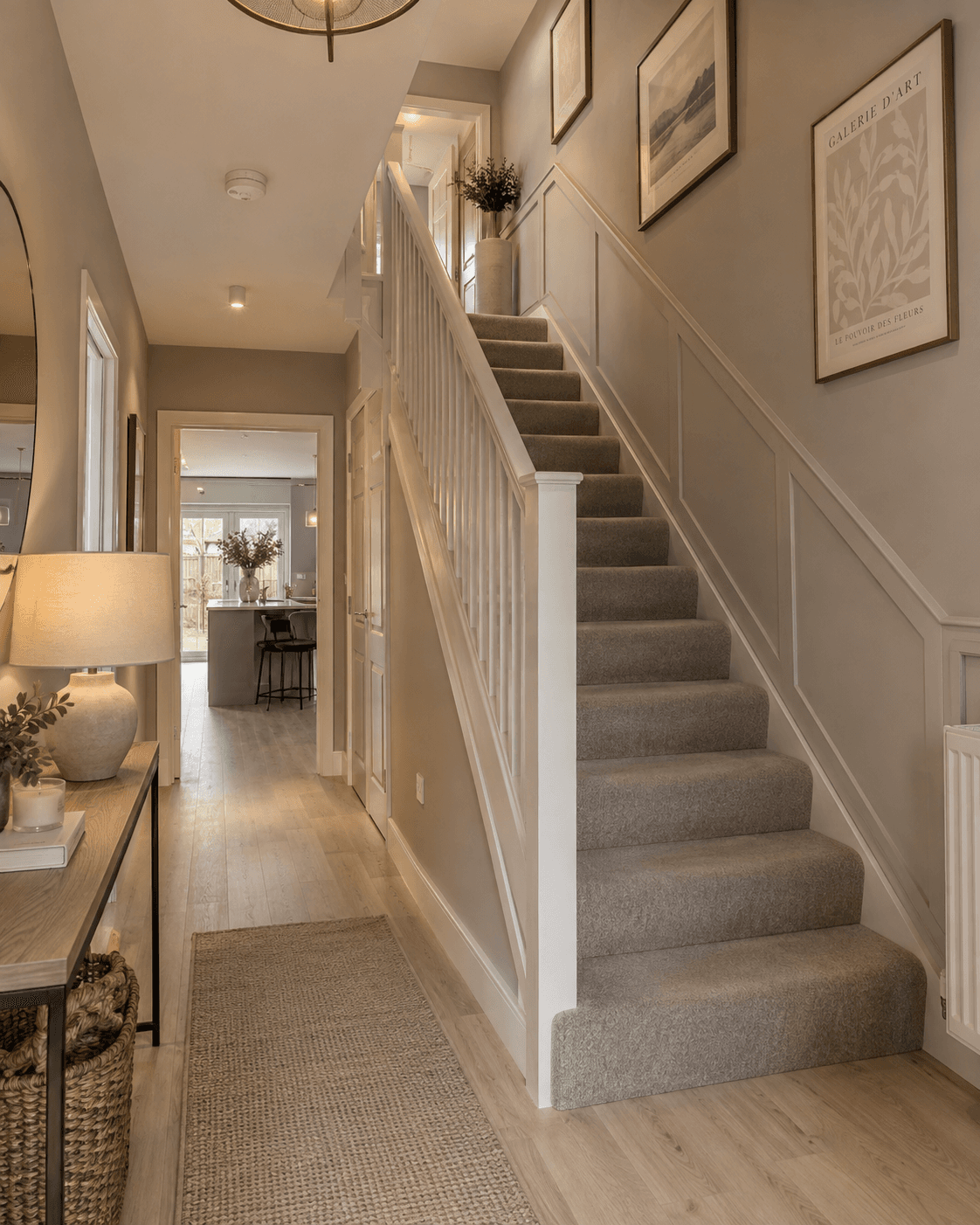 Modern new build hallway with warm taupe walls, neutral carpeted staircase and simple wall moulding continuing up the stairs, creating a more considered, architectural finish.