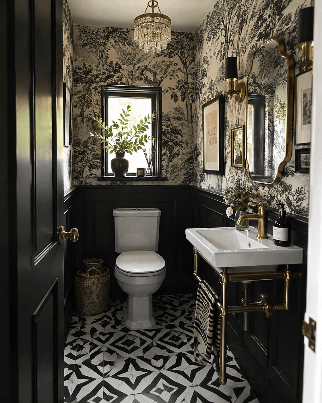 Black and white maximalist downstairs bathroom with bold patterned flooring, botanical wallpaper, black panelling, brass hardware, wall lights and a statement chandelier.