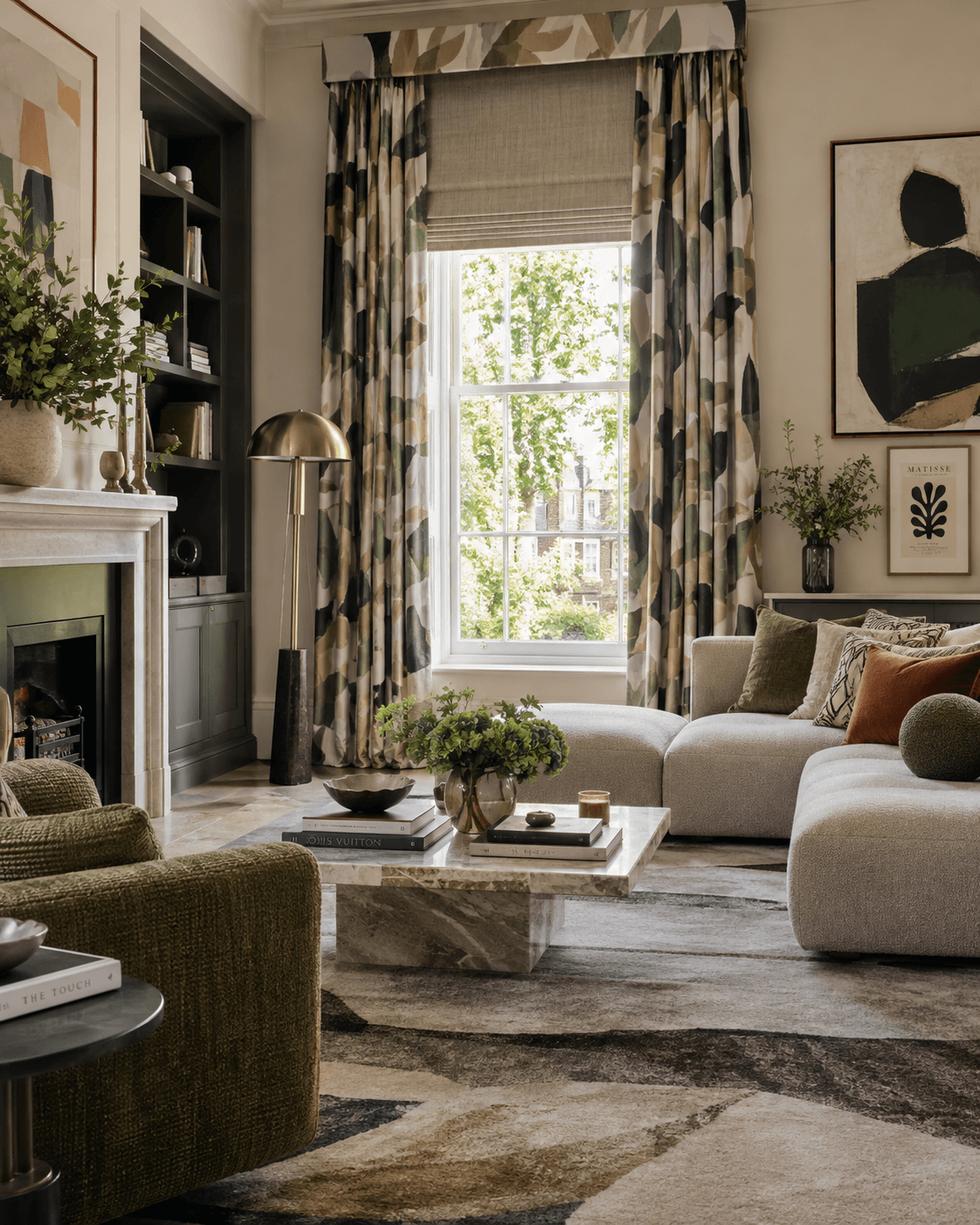 Modern maximalist living room with abstract full length curtains, a tailored pelmet, Roman blind, contemporary artwork, sculptural furniture and layered neutral and olive tones.